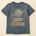 Washed blue t-shirt printed with a retro travel poster of a ringed planet and the word TITAN — flat lay